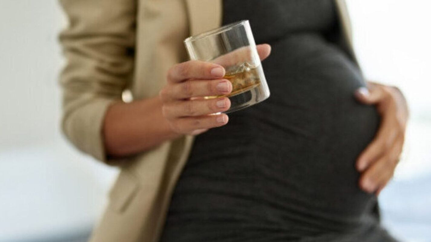A pregnant woman holding a cup of alcohol